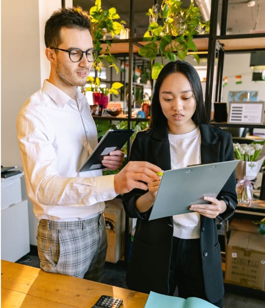 Two colleagues discussing work in a modern office with plants in the background.