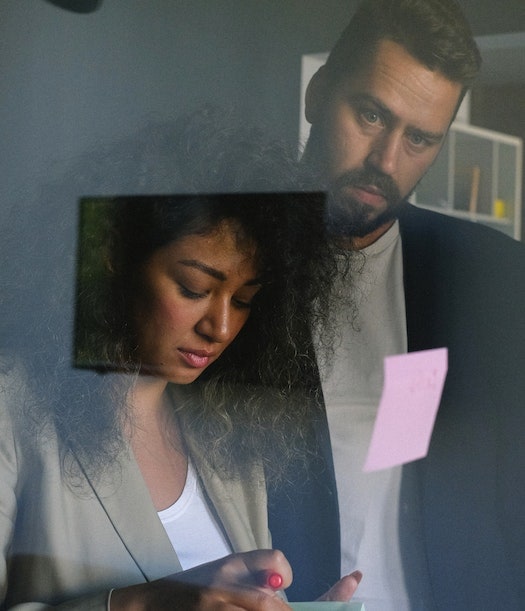 Two people working together, writing notes on sticky notes.