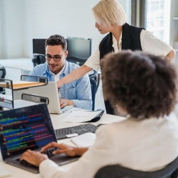 Team of colleagues working together in an office with laptops.